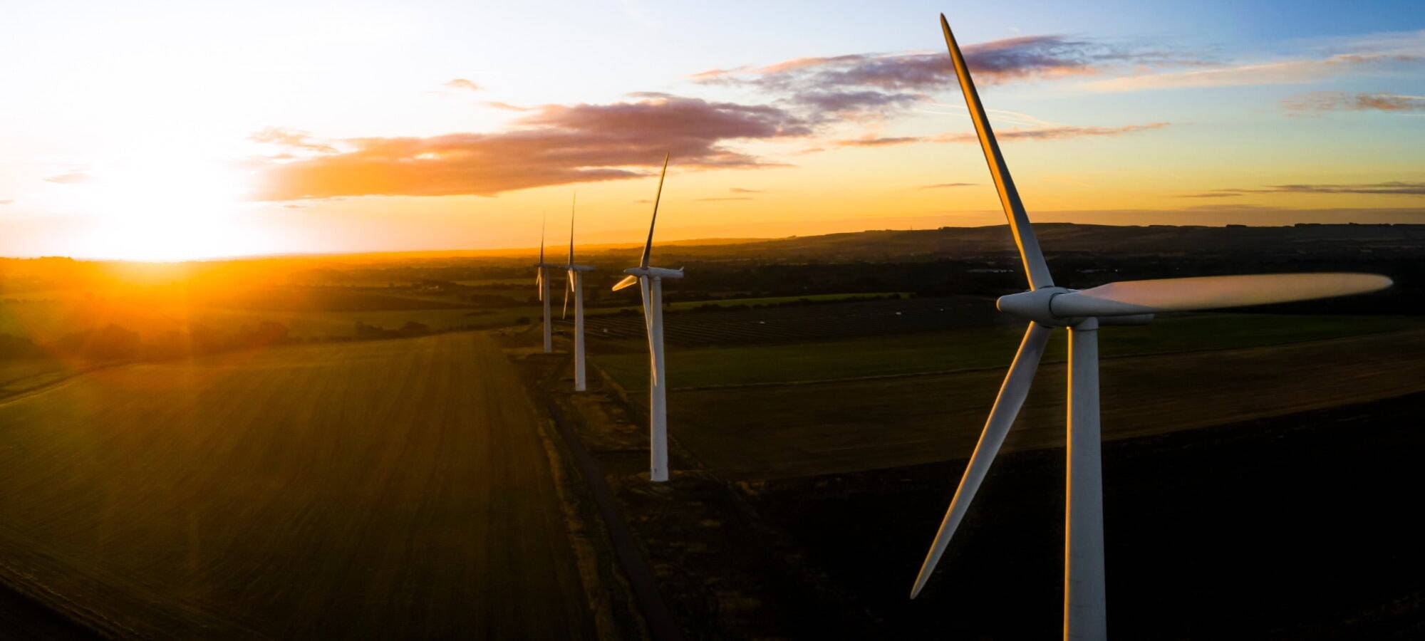 Sonnenuntergang und Windpark mit Wolken und Bergen im Hintergrund ersg